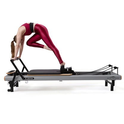 Woman exercising on a Pilates reformer machine on a white background